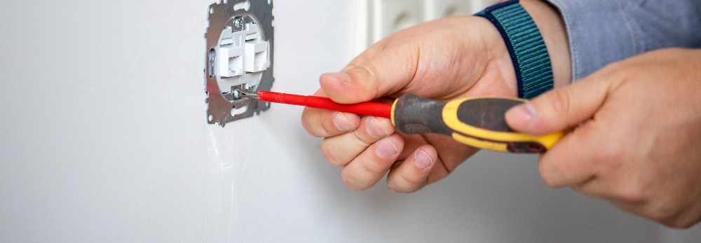 Person montiert Steckdose mit Schraubendreher